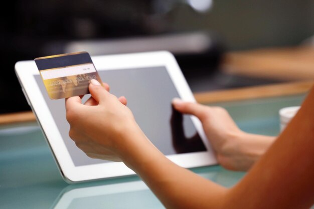 Mãos femininas segurando cartão de crédito com tablet digital na mesa close-up