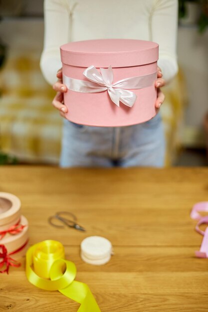 Mãos femininas segurando dão presente rosa com caixa de presente de fita branca