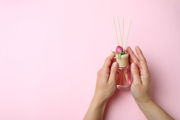 Mãos femininas segurando difusor em fundo rosa