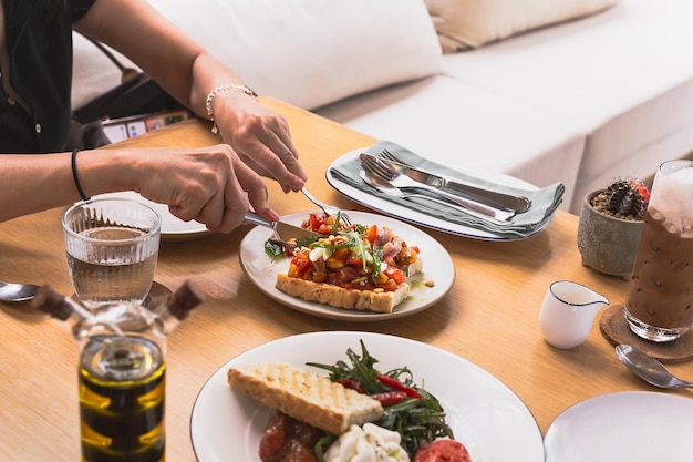 Mãos femininas segurando faca e garfo cortando bruschetta aperitivo no prato