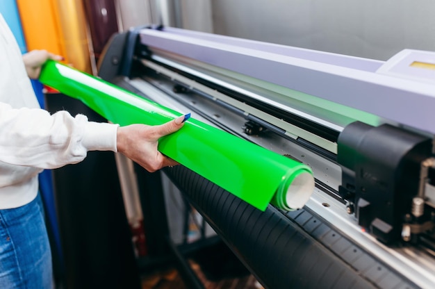 Mãos femininas segurando material verde imprimível em plotter de impressão de grande formato design gráfico e