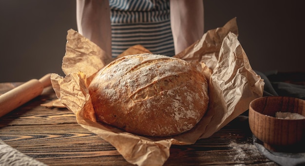 Mãos femininas segurando pão natural caseiro com crosta dourada em um guardanapo em um antigo fundo de madeira estilo rústico