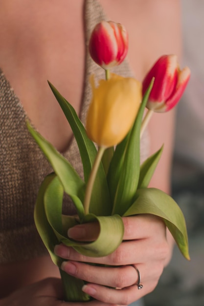 Mãos femininas segurando tulipas de flores de primavera amarelas e rosa Detalhes femininos de beleza