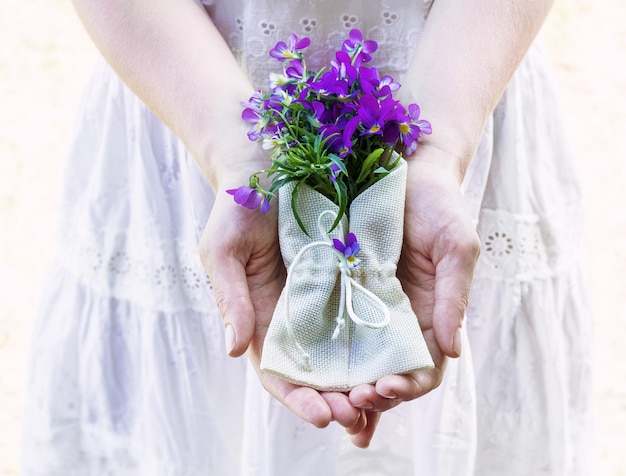 Mãos femininas segurando um buquê de amores-perfeitos de flores em um envelope têxtil Ternura e beleza Foco seletivo