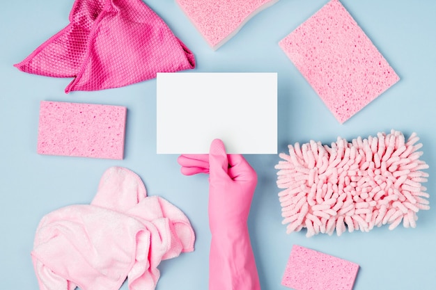 mãos femininas segurando um cartão vazio de fundo azul com detergentes e acessórios de limpeza