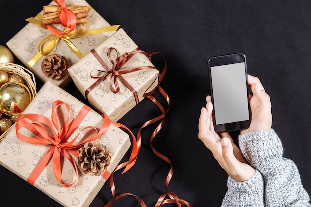 Foto mãos femininas segurando um celular em branco com presentes de natal