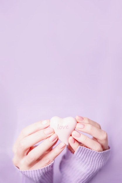 Mãos femininas segurando um coração rosa pálido no violeta, copie o espaço