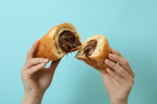 Mãos femininas segurando um croissant com chocolate no azul