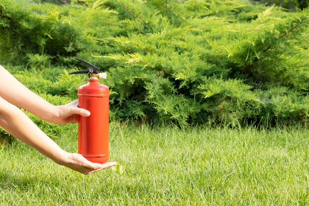 mãos femininas segurando um extintor de incêndio vermelho no jardim