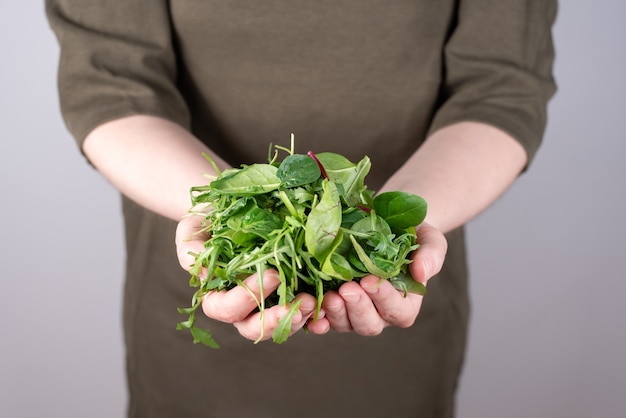 Mãos femininas segurando um monte de vegetais folhosos em um gramado