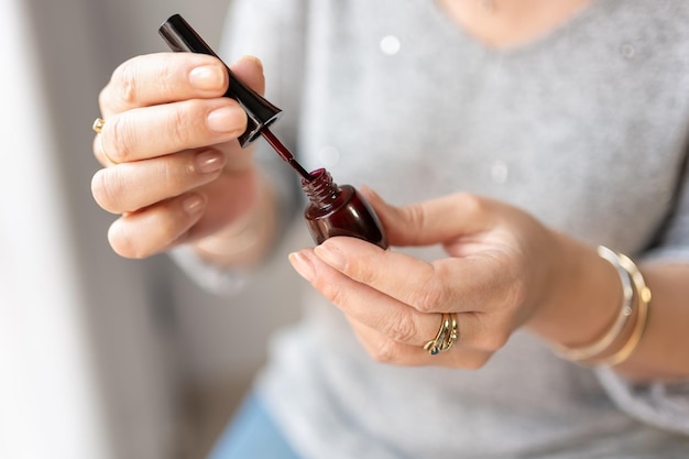 Mãos femininas segurando um pequeno frasco de esmalte preparado para pintar as unhas