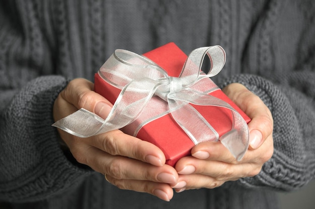 Mãos femininas segurando um presente vermelho embrulhado com fita de prata Presente de Natal na época do Natal