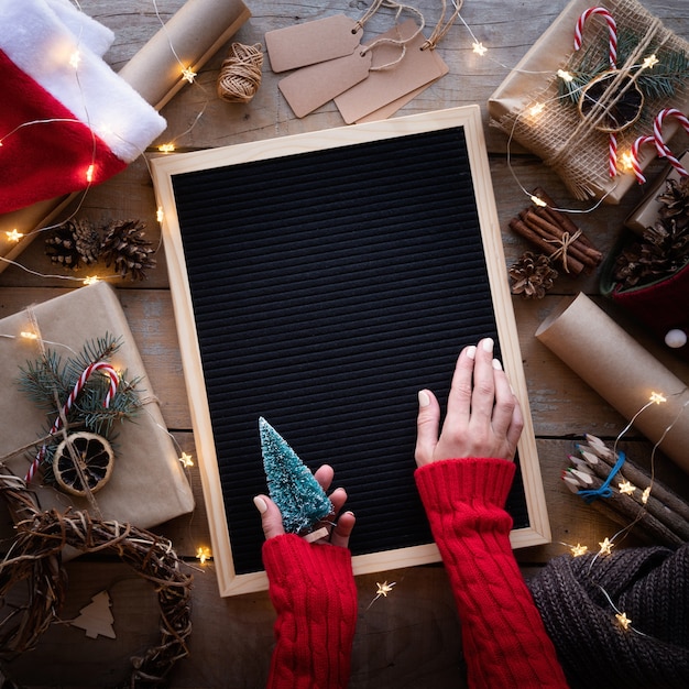 Mãos femininas segurando um quadro de carta em branco com presentes de Natal na horizontal