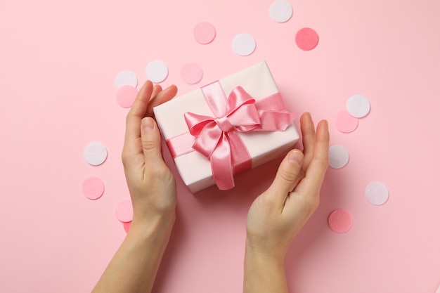 Mãos femininas segurando uma caixa de presente em fundo rosa