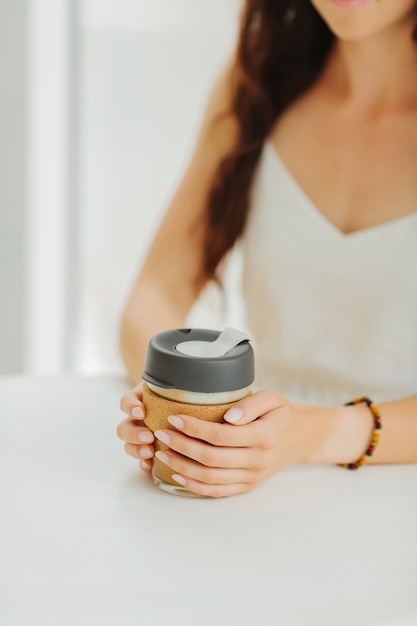 Mãos femininas segurando uma caneca de café reutilizável em uma cafeteria. estilo de vida sustentável. conceito ecológico.