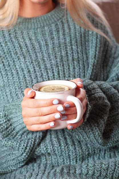 Mãos femininas segurando uma caneca de chá quente com limão de manhã. Mulher jovem relaxante xícara de chá nas mãos.