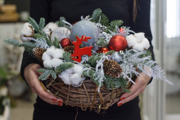 Mãos femininas segurando uma composição de ano novo de ramos de pinheiro, decorações de Natal e velas, presente