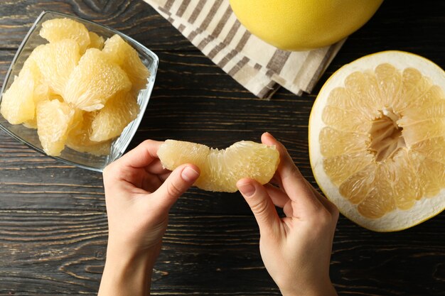 Mãos femininas segurando uma fatia de pomelo na mesa de madeira com pomelo maduro