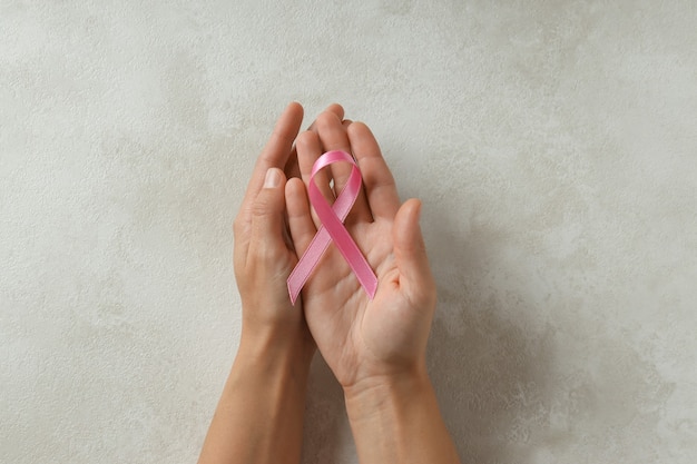Mãos femininas segurando uma fita de conscientização do câncer de mama em um plano de fundo texturizado