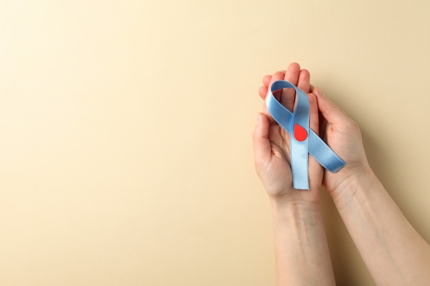 Mãos femininas segurando uma fita de conscientização sobre diabetes em fundo bege