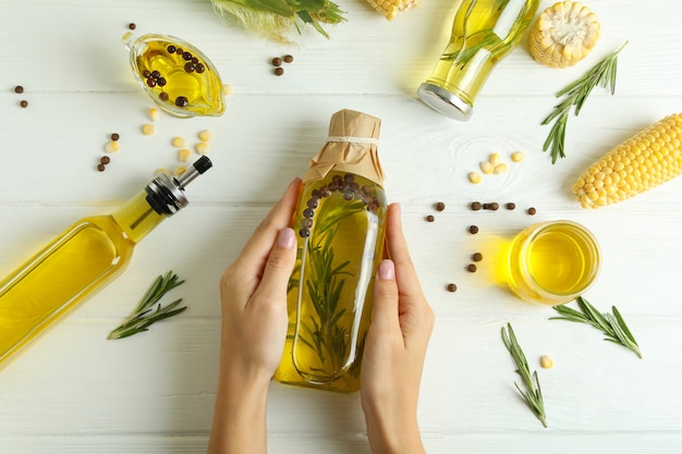 Mãos femininas segurando uma garrafa de óleo em fundo branco de madeira com ingredientes