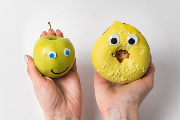 Foto mãos femininas segurando uma maçã e donut com caretas e olhos enormes. conceito de nutrição adequada.