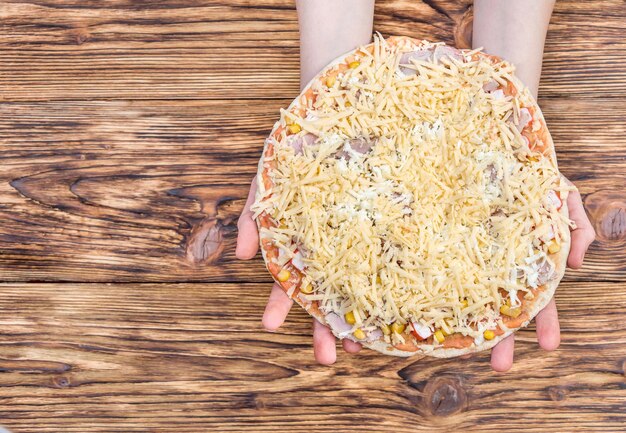 Mãos femininas segurando uma pizza crua vista superior