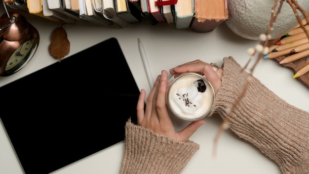 Mãos femininas segurando uma xícara de café com creme