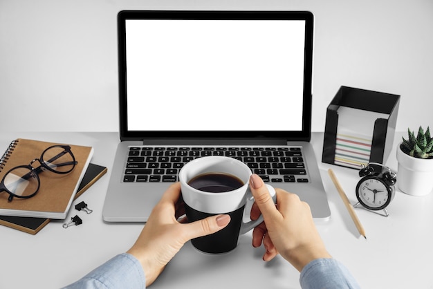 Mãos femininas segurando uma xícara de café e um laptop com uma tela em branco