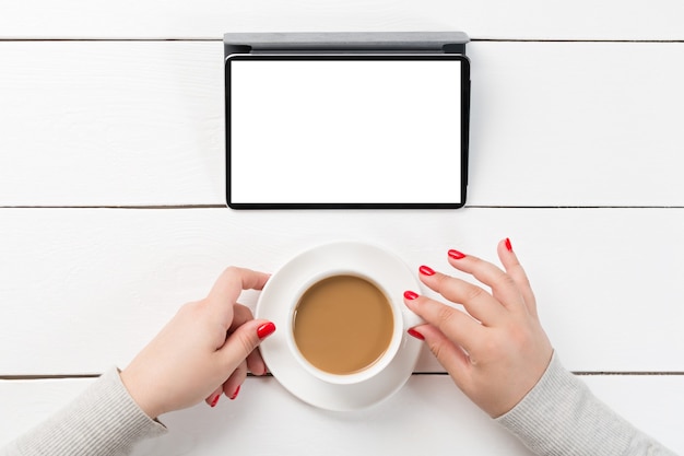 Mãos femininas segurando uma xícara de café na mesa de madeira com computador tablet digital.