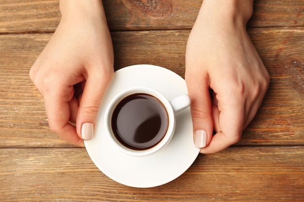 Mãos femininas segurando uma xícara de café no fundo de madeira