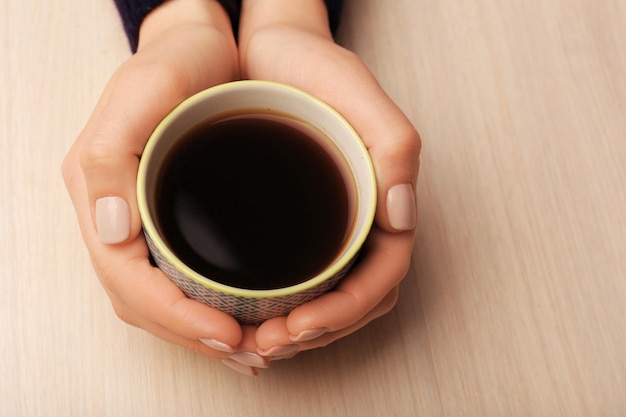 Mãos femininas segurando uma xícara de café no fundo de madeira