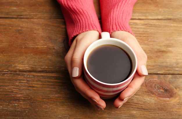 Mãos femininas segurando uma xícara de café no fundo de madeira