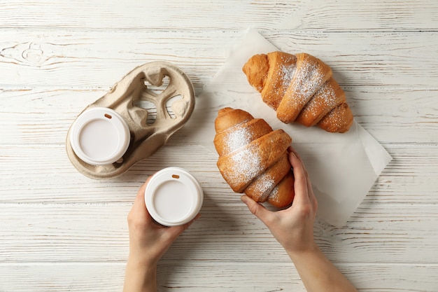Mãos femininas segurar a xícara de café e croissant em fundo de madeira, vista superior
