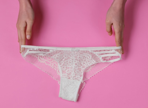 Mãos femininas segurar calcinha de renda sexy em um fundo rosa. Foto de estúdio