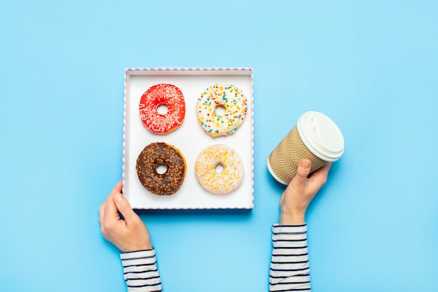 Mãos femininas segurar uma caixa com donuts, uma xícara de café em um azul. loja de confeitaria conceito, bolos, café.