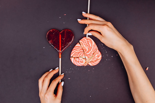 Mãos femininas tentando coletar doces quebrados na forma de um coração