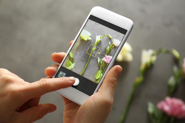 Mãos femininas tirando foto de lindas flores com smartphone