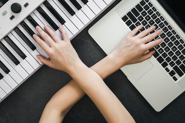 Foto mãos femininas tocando teclas de sintetizador e trabalhando em um laptop