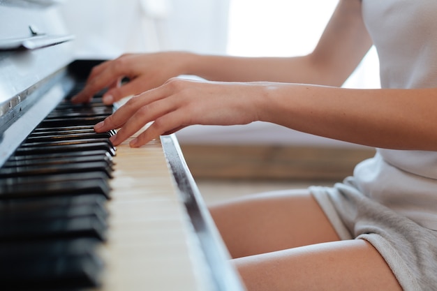 Mãos femininas tocando teclas pretas e marfim enquanto tocam música clássica no piano em casa