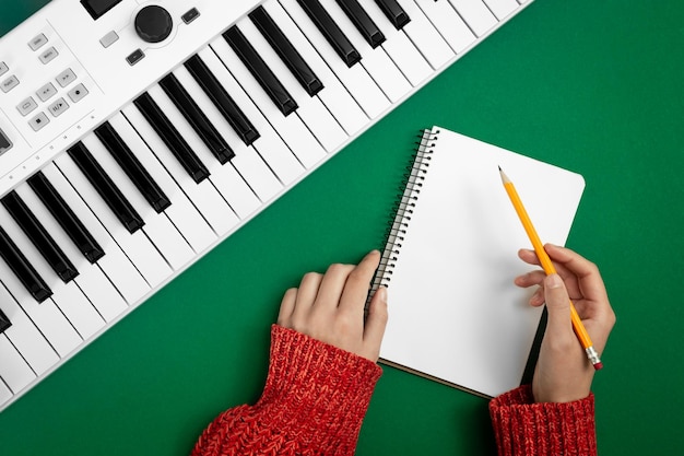 Mãos femininas vazias notepad e teclas de música em fundo verde vista superior conceito de criatividade musical