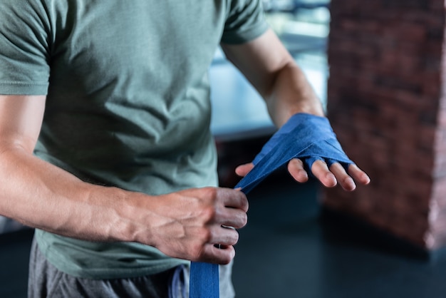 Mãos fortes. Perto das mãos fortes de um esportista treinando na academia usando faixas de pulso azuis compridas