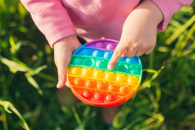 mãos garotinha segurando um brinquedo anti-stress pop em pé ao ar livre na natureza