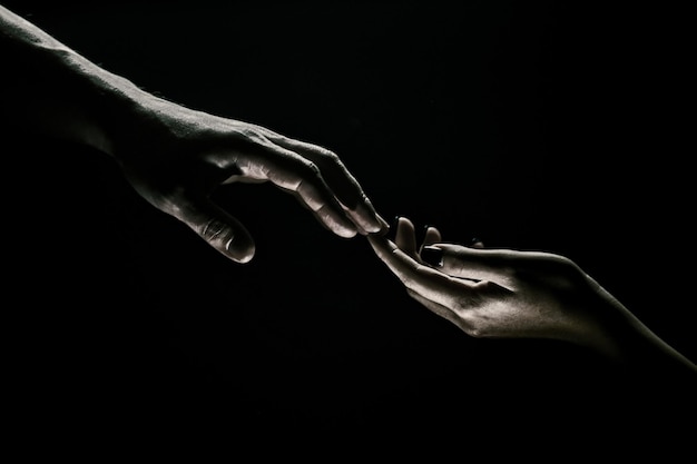 Mãos gesticulando em fundo preto dando um apoio de mão amiga e ajudando as mãos de salvação de dois pe