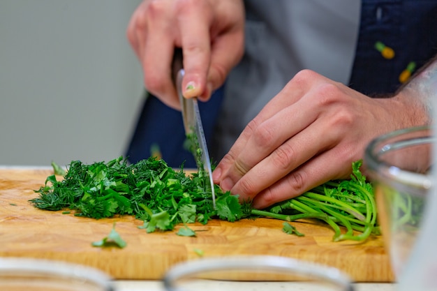 Mãos humanas com faca de aço afiada shredding folhas de salsa verde na placa de madeira