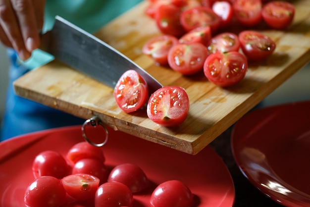 Mãos humanas cortam e cortam tomates na tábua de cortar salada de legumes para jantar ou comida saudável