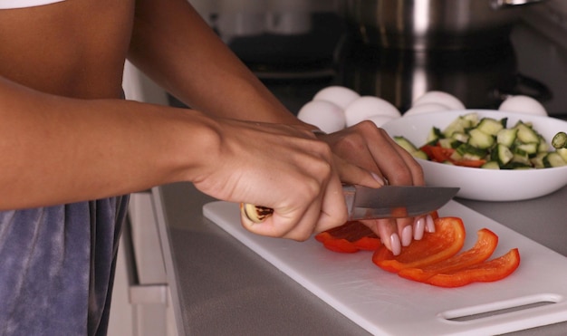 Mãos humanas cozinhando salada de legumes na cozinha.