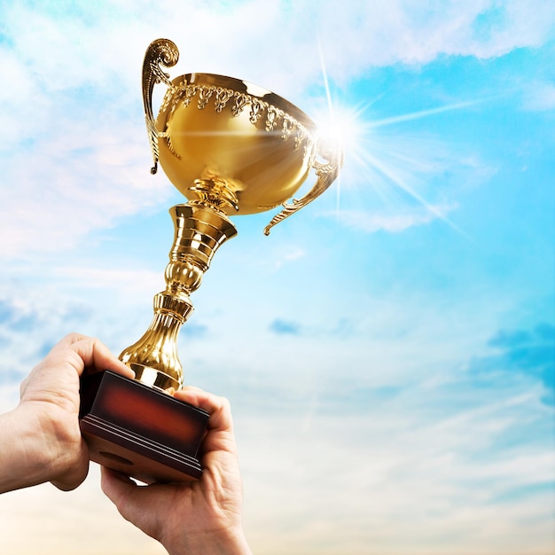 Mãos humanas de close-up segurando o troféu de ouro no fundo