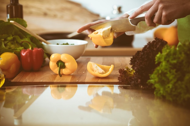 Mãos humanas desconhecidas cozinhando na cozinha. Mulher cortando pimenta amarela. Refeição saudável e conceito de comida vegetariana.