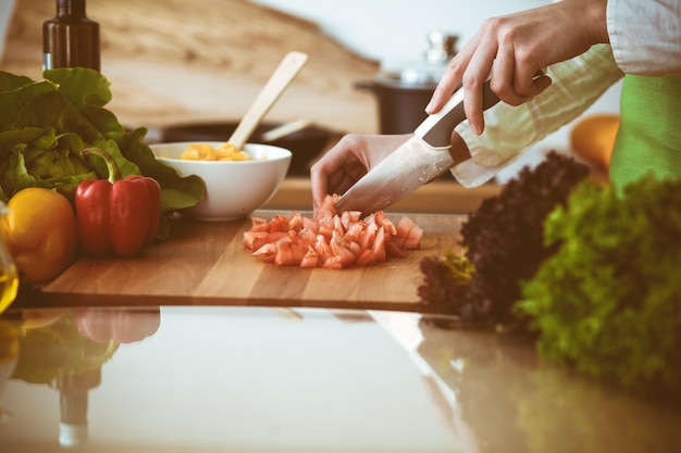 Mãos humanas desconhecidas cozinhando na cozinha. Mulher cortando tomates vermelhos. Refeição saudável e conceito de comida vegetariana.